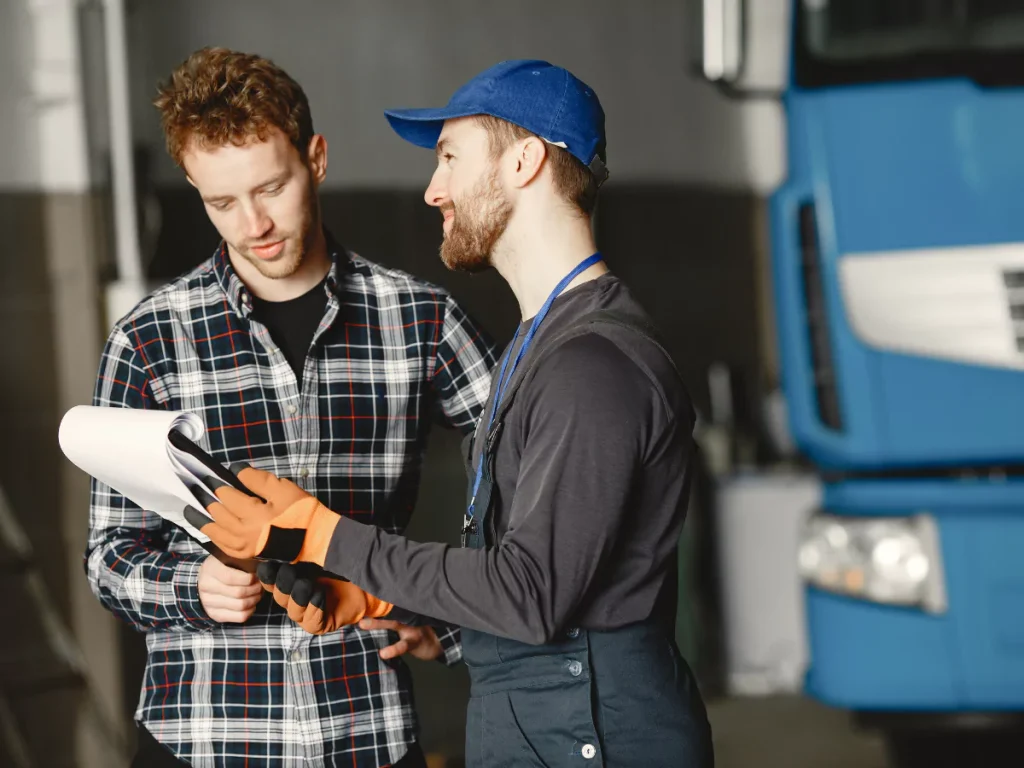 A gloved technician in a cap explains vehicle inspection results to a customer, showcasing certified inspection services in Champions Park.
