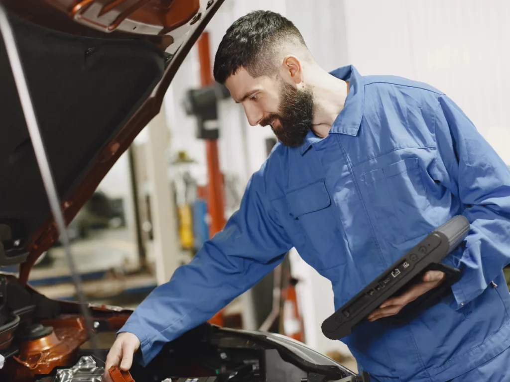 A technician conducting a mobile auto evaluation in Lakewood Place, checking the engine with a handheld tool.