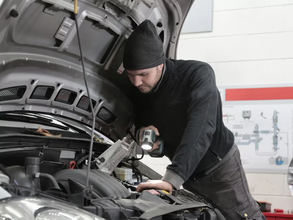 A skilled mobile auto inspection mechanic in Houston using a flashlight to check a car's engine bay.
