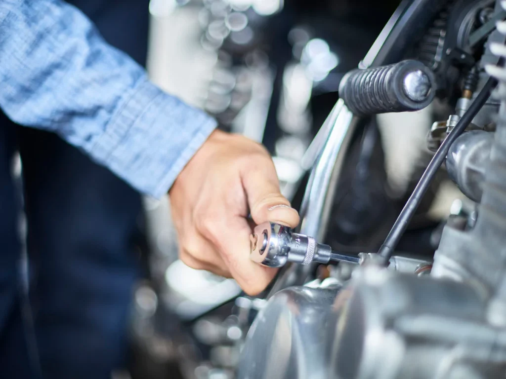 Motorcycle emissions inspection at Heron Lakes Estates, a technician's hand adjusting a part on a motorbike.