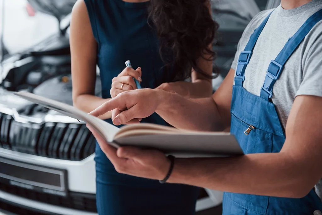 Detailed PPI inspection houston on a car engine being performed by auto technician and discussing notes with female client.
