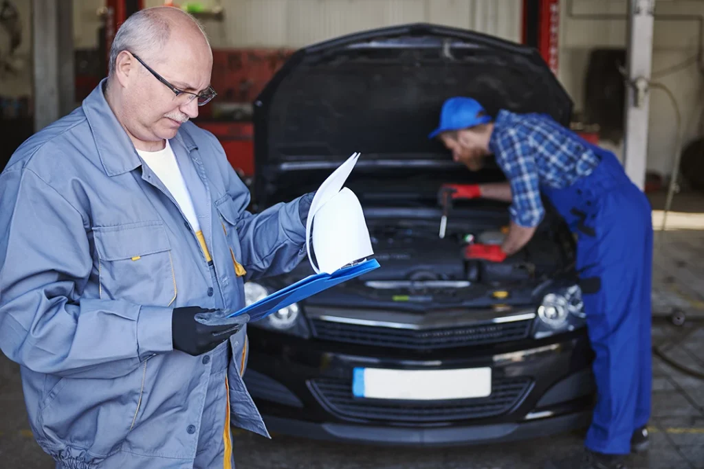 Two mechanics working on pre-purchase vehicle in Houston with open hood and reading notes.