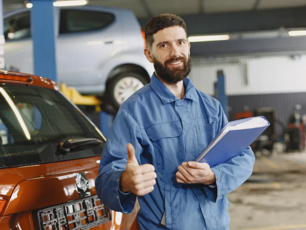 A friendly mechanic in a blue uniform, holding a clipboard next to a red car, symbolizing comprehensive third-party inspection services in Houston.