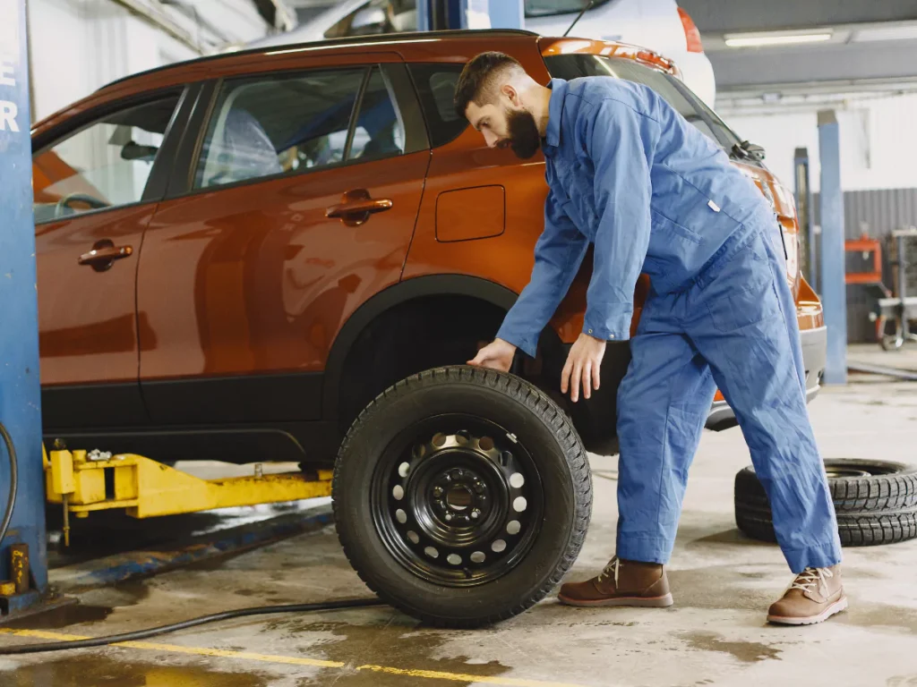 A male automotive technician carefully examining the wheel and tire of a vehicle during a comprehensive third-party inspection service in Houston.