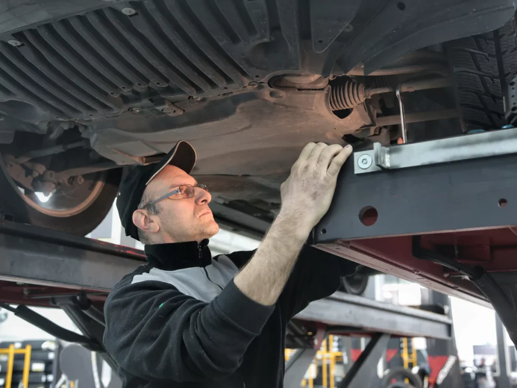 A skilled mechanic performing an undercarriage inspection on a lifted vehicle, representing third-party quality services in Champions Park.