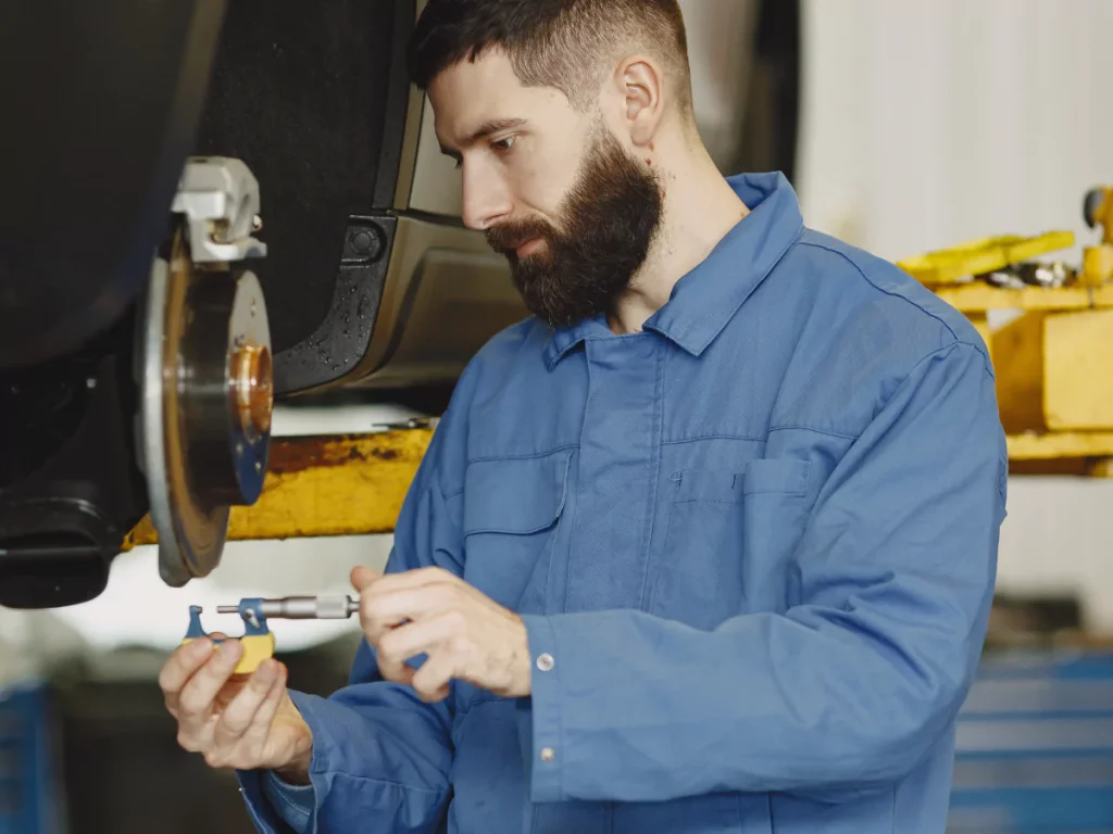 Professional used car inspection services in Houston, a mechanic in a blue jumpsuit carefully checking a car part.