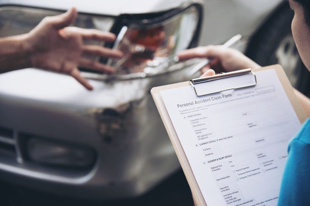 Person filling out accident claim form near damaged car after pre purchase inspection in Houston.
