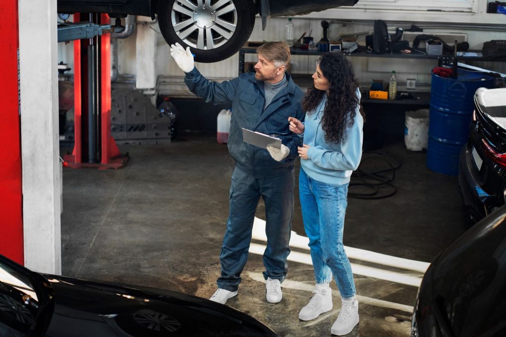 A mechanic and client discuss a pre purchase used car inspection Houston, inspecting a lifted car wheel in a garage.
