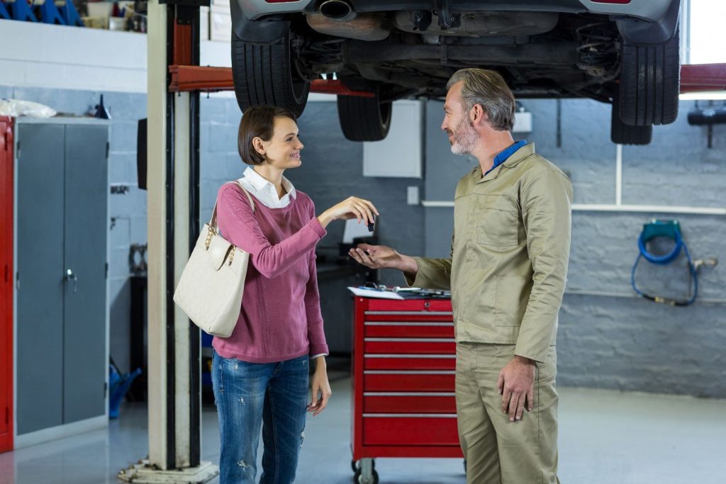 Woman receiving car keys from mechanic after third party inspection in Houston garage.