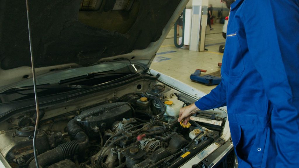 Mechanic performing third party inspection on a car's engine in Houston, checking oil dipstick for maintenance and safety.