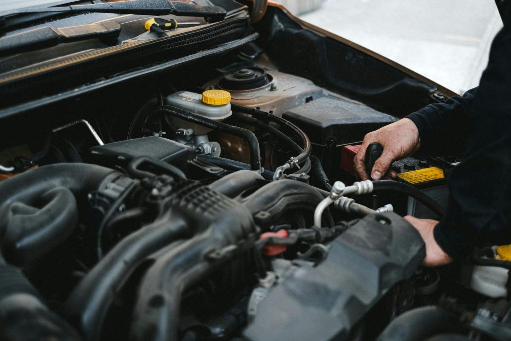 Mechanic conducting third party inspection on a car engine in Houston, checking battery and fluids for safety and quality.