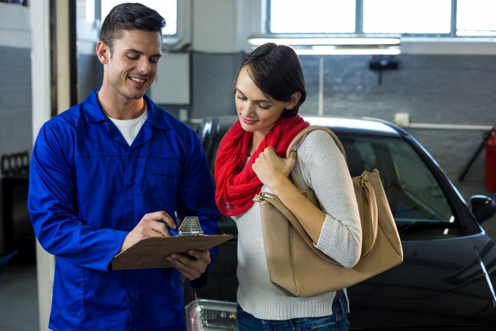 Mechanic discussing checklist with female customer beside car in Houston third party inspection garage.