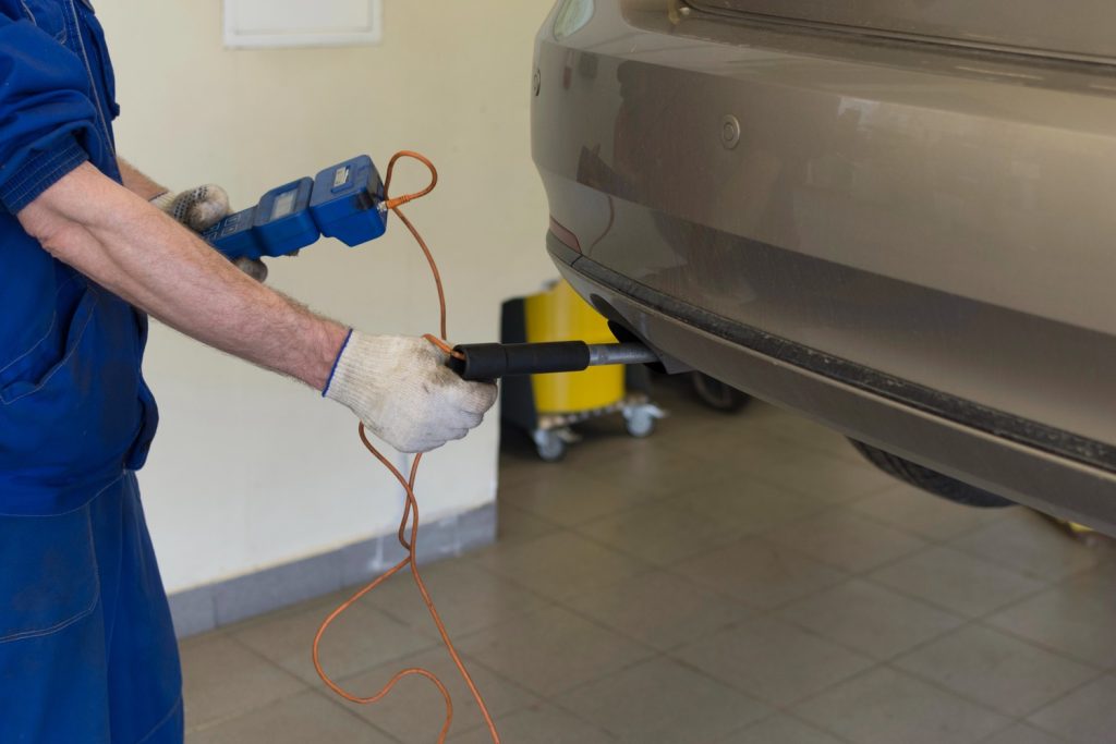 Mechanic performing check used car service Houston with diagnostic tool on a gray car in a garage.