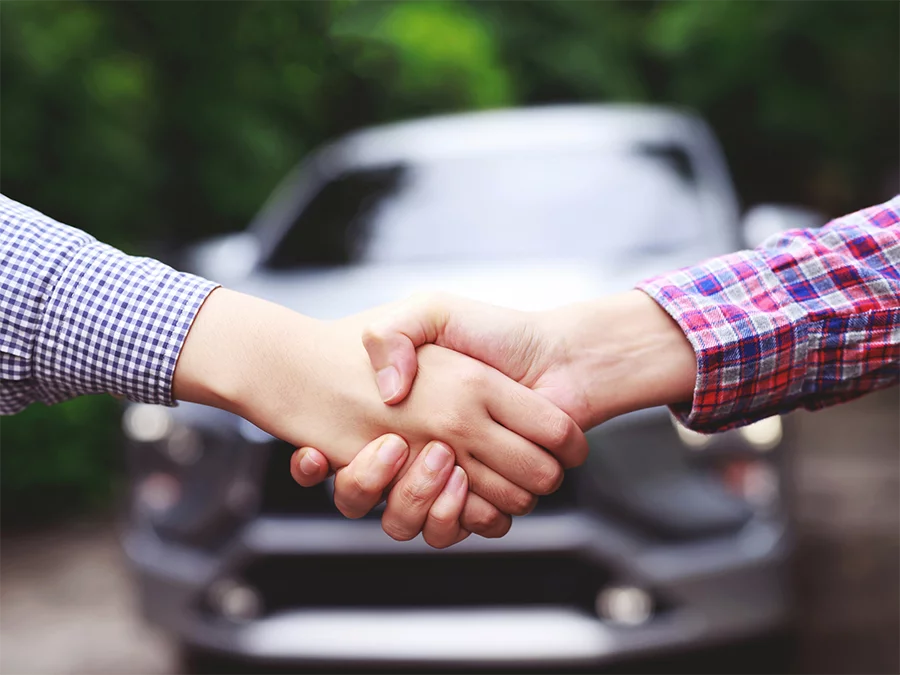 Two people shaking hands in front of a car after check used car service in Houston.