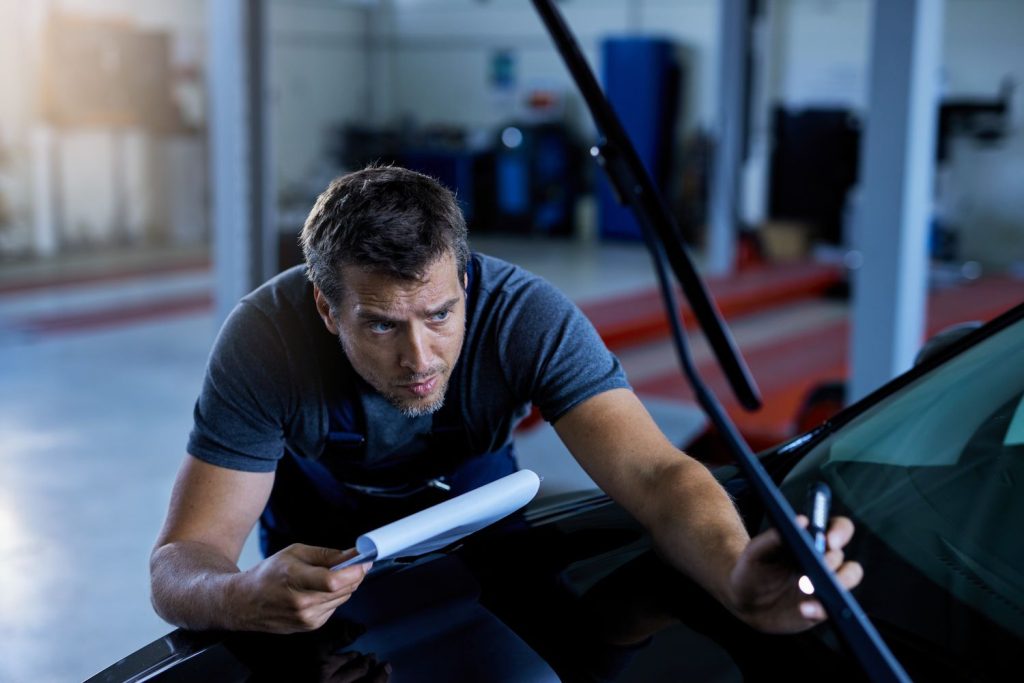 Mechanic examining car windshield wiper with report during pre purchase inspection in Houston garage.