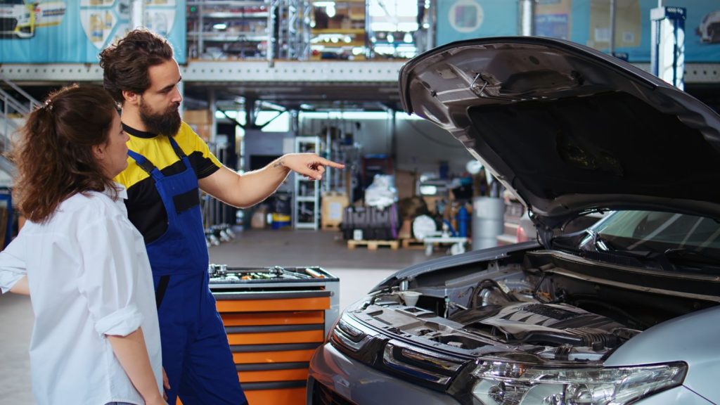Mechanic pointing at car engine while discussing with client in Houston third party inspection garage.
