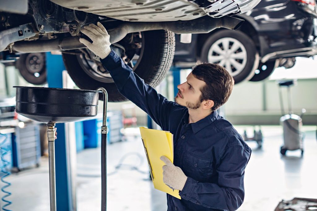Mechanic inspecting car undercarriage with checklist for used auto inspection Houston.
