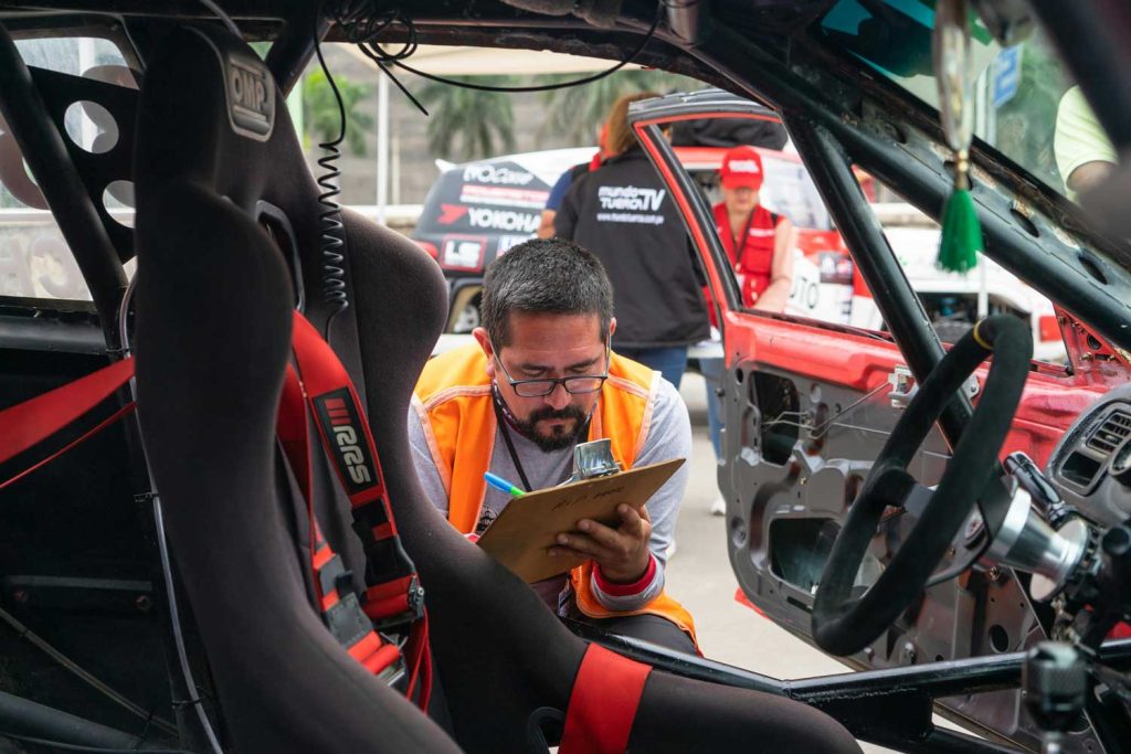Technician inspecting a red car's undercarriage during Pre Purchase Used Car Inspection Houston, with a lift and tools visible.