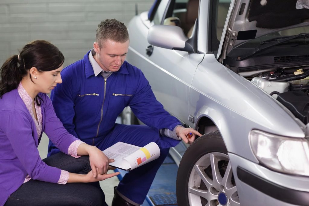 Client and mechanic inspecting car tire with report during third party inspection in Houston garage.