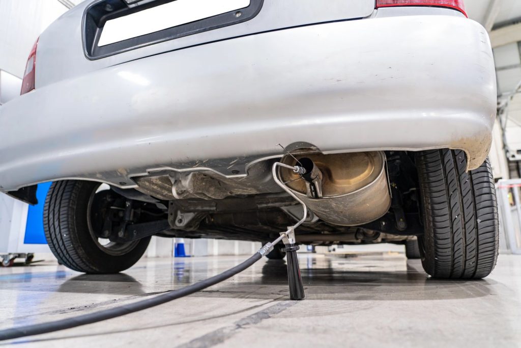 Technician performing check used car service Houston on a silver car's exhaust system in a garage.