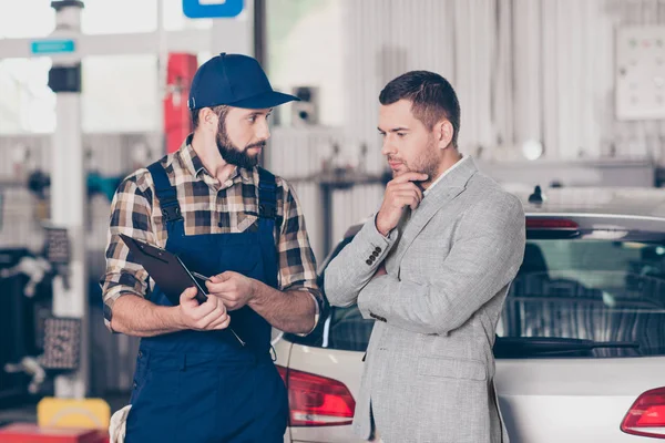 Technician inspecting a gray car's suspension during Pre Purchase Used Car Inspection Houston, with a lift and tools in view.