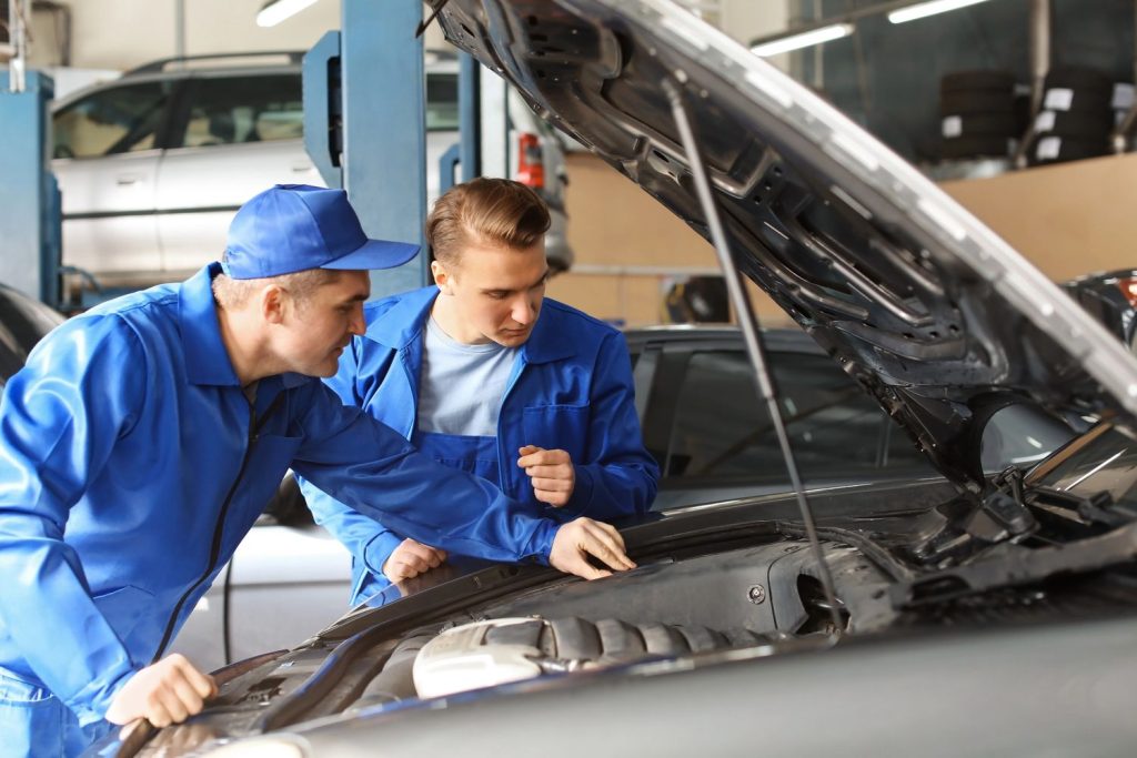 Two mechanics conducting a third party inspection of a vehicle engine in an automotive garage.