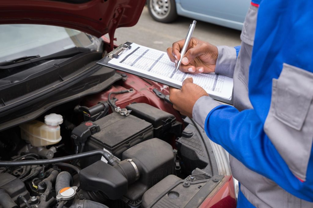 Mechanic performing used auto inspection Houston on car engine with checklist.