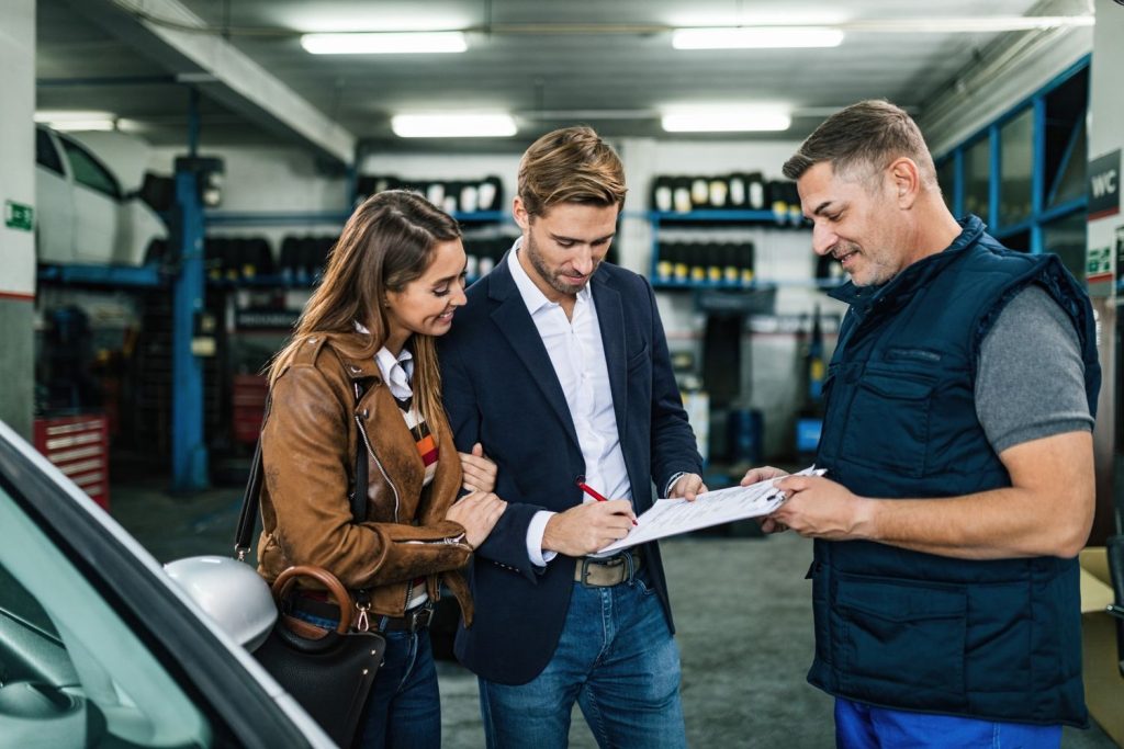 Couple consulting with mechanic on clipboard during a Pre Purchase Inspection Houston, ensuring vehicle safety and condition.