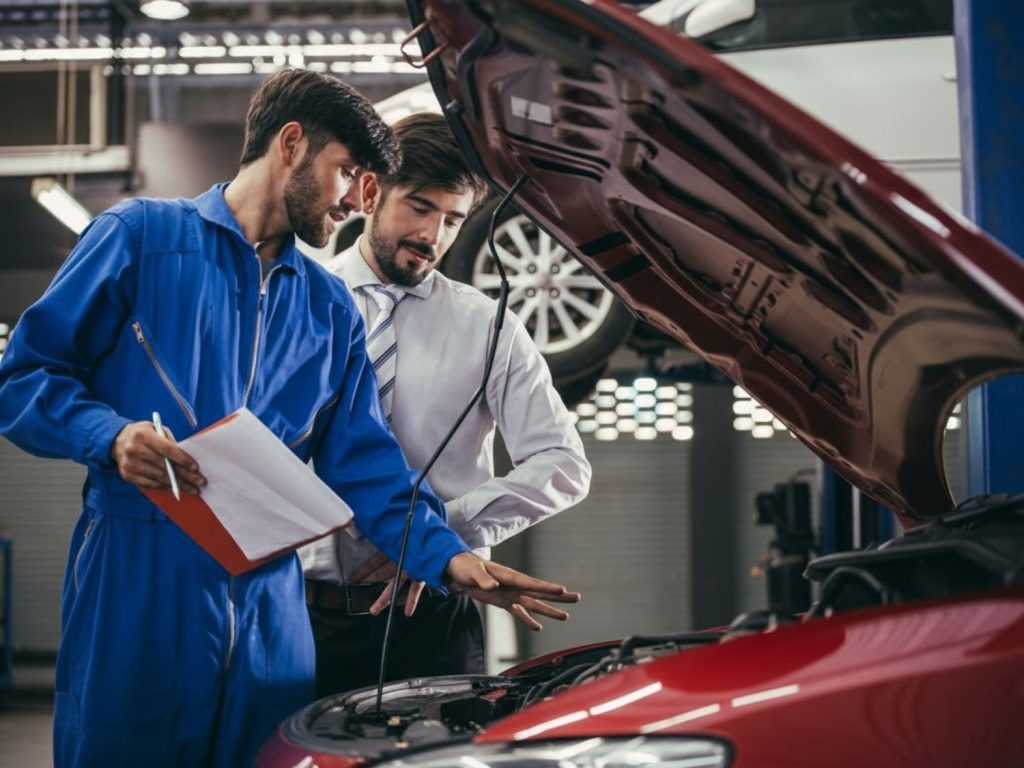 Two mechanics reviewing a checklist over an open car hood at a top vehicle inspection service in Houston, ensuring quality auto checks.