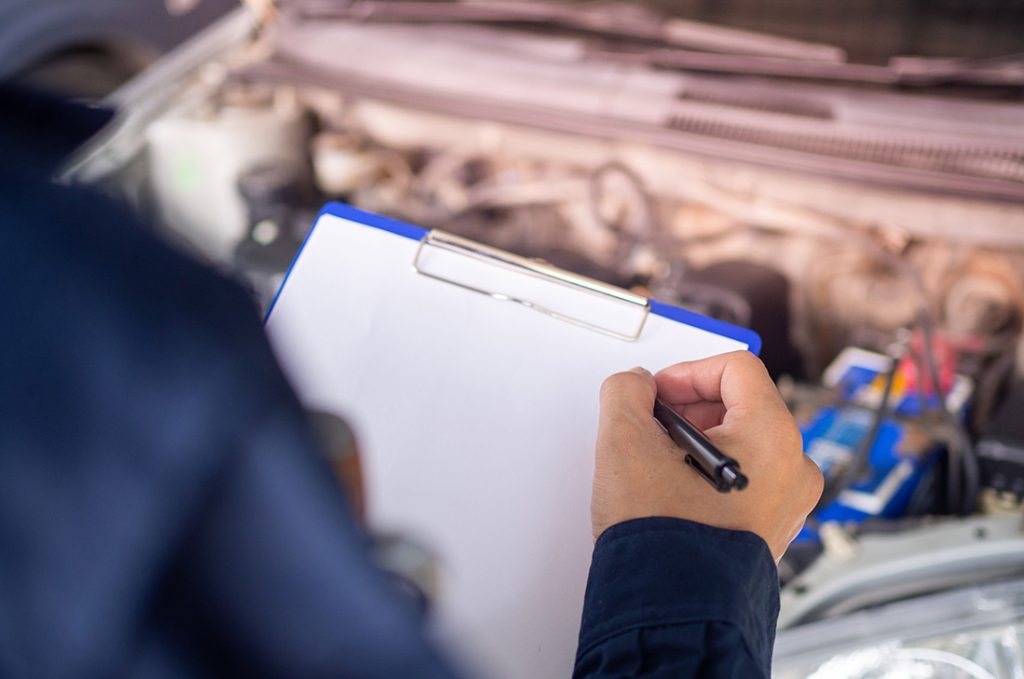 Inspector checking an engine bay and filling out forms for a mobile car check Houston on-site.