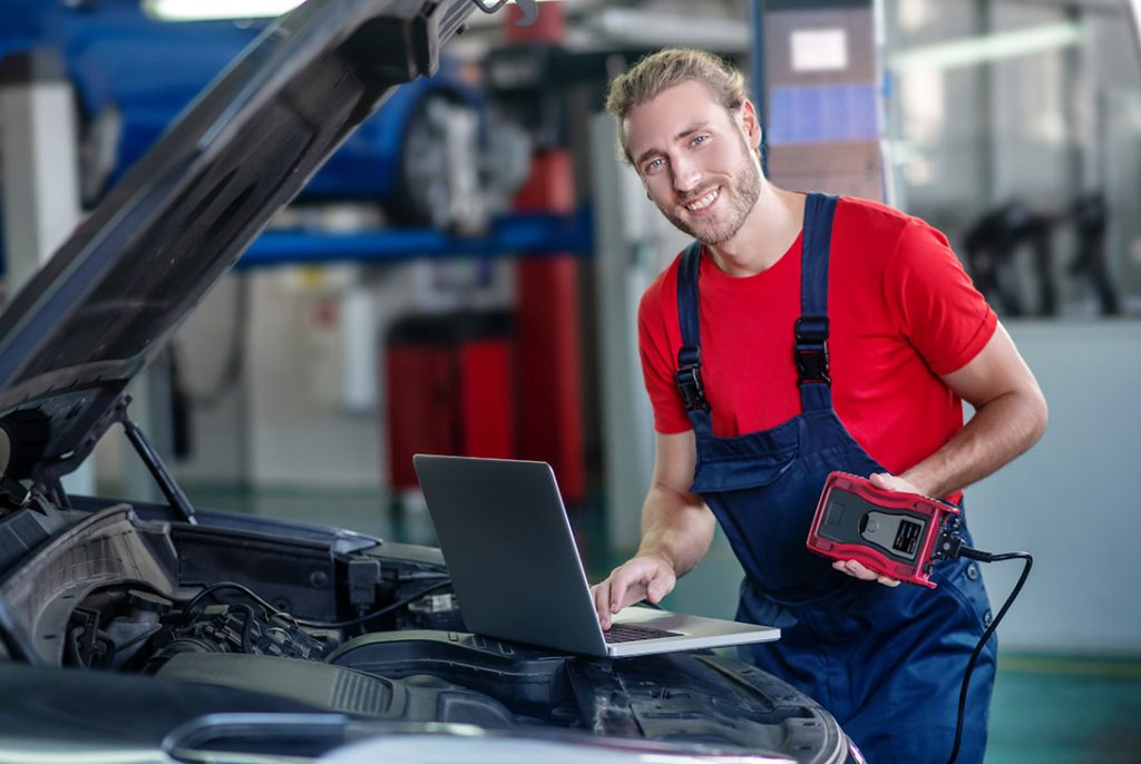 Smiling inspector using a laptop for diagnostics at a vehicle inspection service Houston workshop.