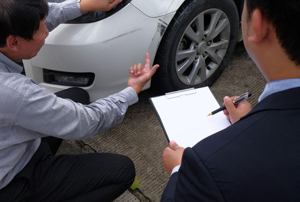 Expert certified third party car inspector pointing out damage on a white car's bumper to a client.