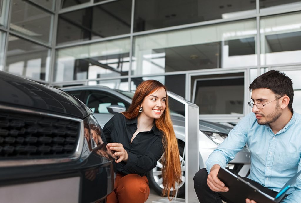 Buyer and seller reviewing the final third party car inspection with report for a used black vehicle.