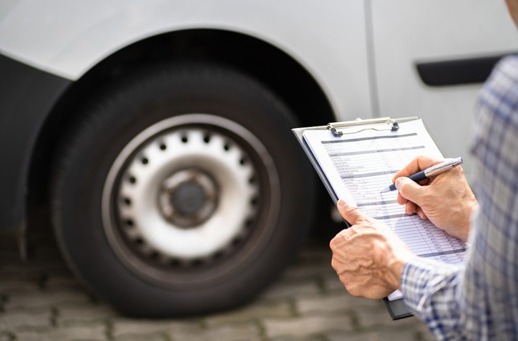 Close-up of a hand filling out a checklist for a used car by a certified third party car inspector.