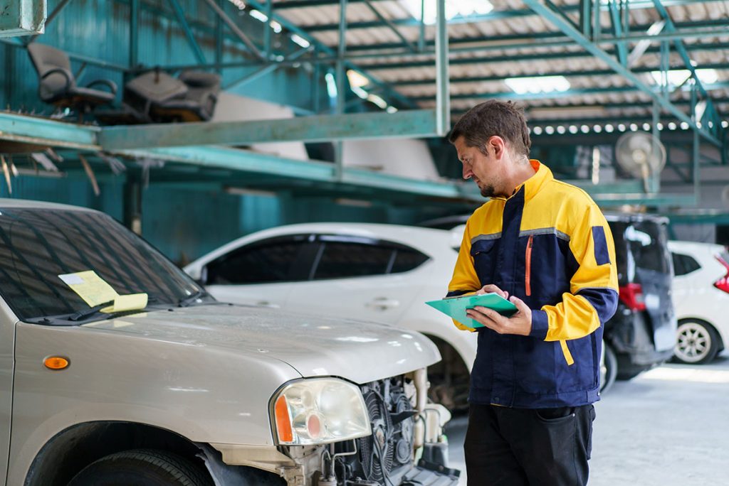 Mechanic conducting a pre-purchase third party car inspection with report on a used vehicle in an auto garage.