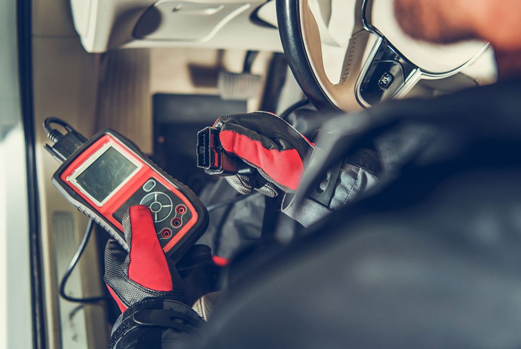 Technician connecting a diagnostic tool for a professional used car inspection service inside a car.