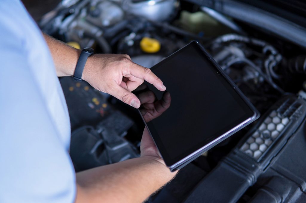 Technician using a tablet over the engine bay for an urgent same day pre purchase car inspection.