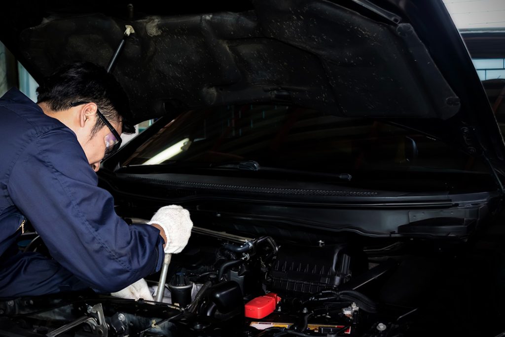 Mechanic performs detailed before you buy car inspection Houston under the hood, checking the engine and components.