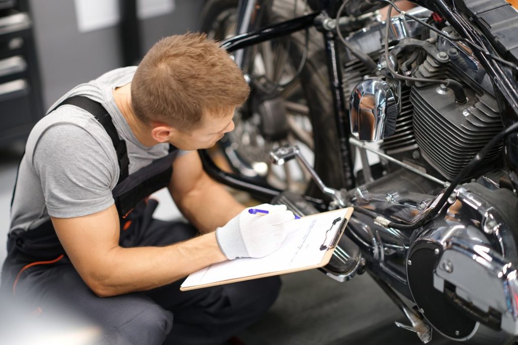 Mechanic completing a detailed motorcycle inspection Houston checklist for a cruiser engine at a local repair shop.