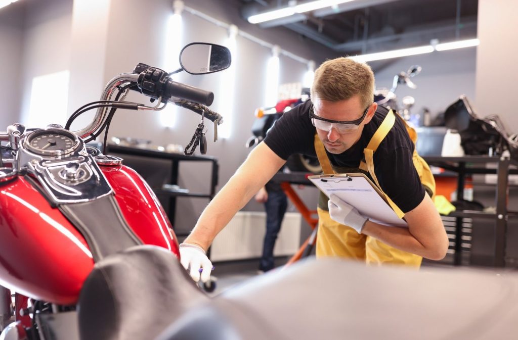 Professional motorcycle inspection Houston technician examining a red bike's fuel tank and controls in the garage.
