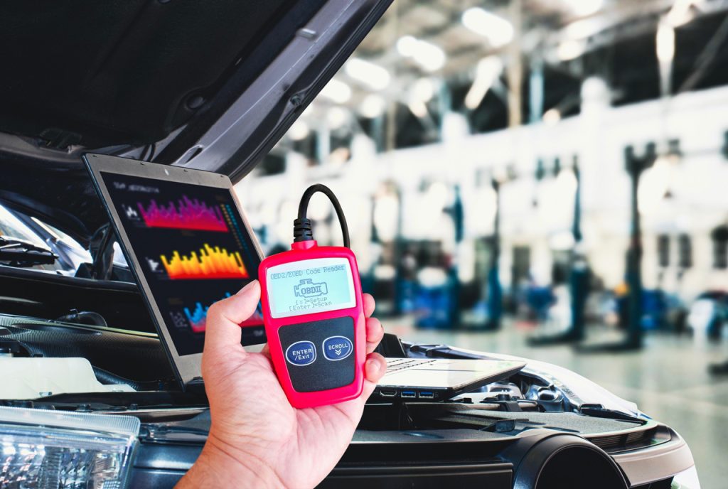 Hand using an OBD2 scanner to check used car service Houston options for engine diagnostics in a professional garage.