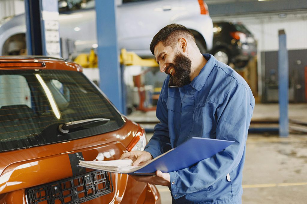 Happy mechanic to check used car before buying holding a service report folder in a professional automotive garage.