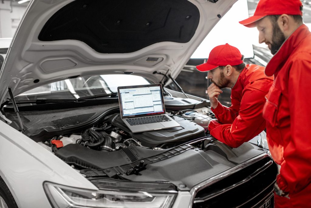 Expert team performing an independent third party auto inspection while analyzing engine data on a laptop screen.