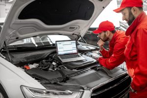 Expert team performing an independent third party auto inspection while analyzing engine data on a laptop screen.
