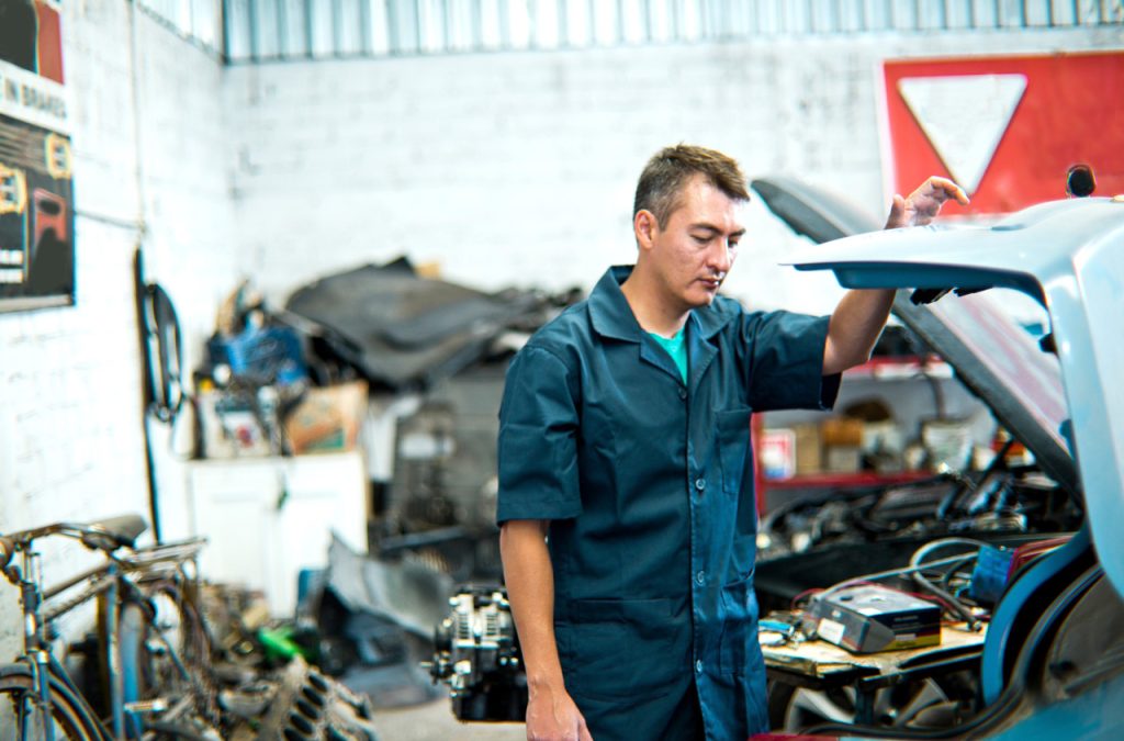 Professional mechanic examining a car undercarriage during an independent third party auto inspection in a modern garage.