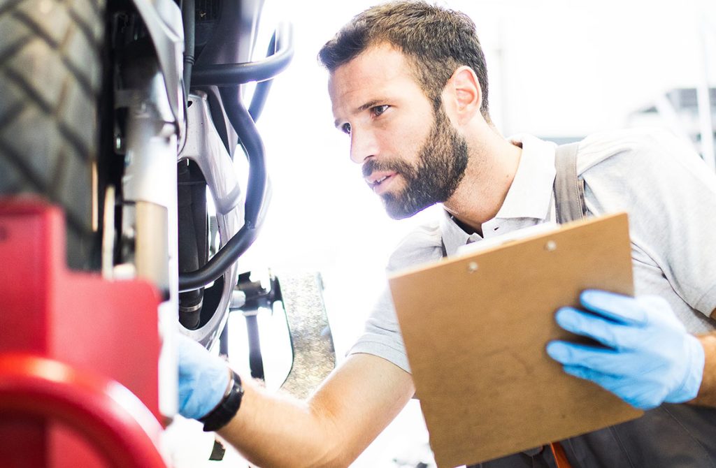 Expert mechanic performing an on-site used car inspection by checking the undercarriage and tires for safety.