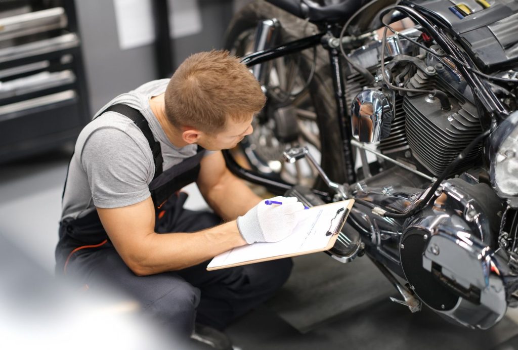 Professional motorcycle mechanic performing a multi-point safety inspection and diagnostic on a cruiser in a repair shop.