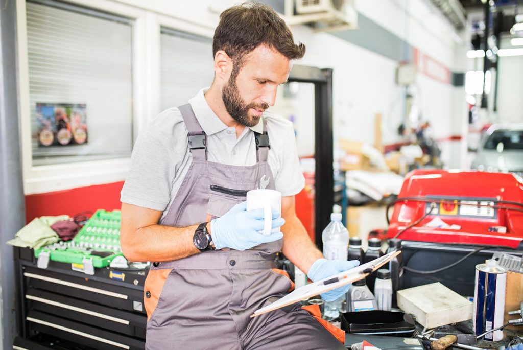 Professional mechanic reviewing a detailed report during an on-site used car inspection at a local service garage.