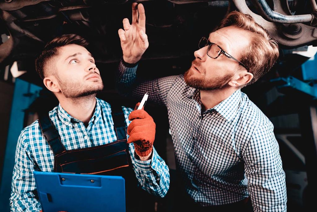 Two mechanics conducting an undercarriage diagnostic for an on-site used car inspection to ensure vehicle safety.