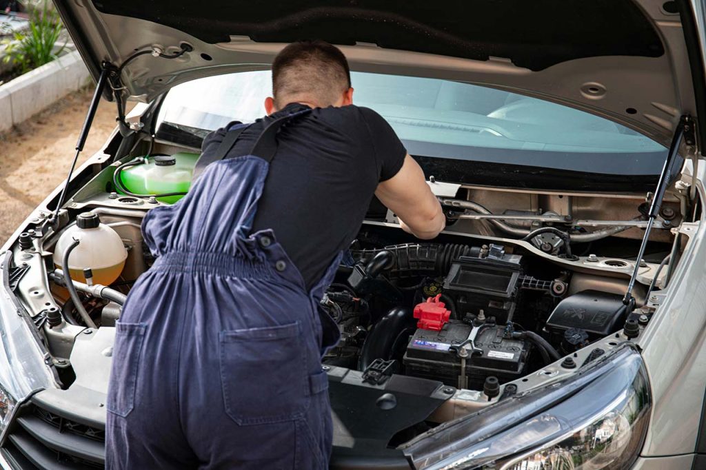 Professional mechanic to check used car before buying by inspecting the engine components under a silver hood.